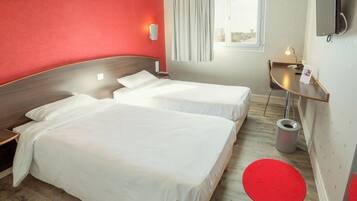 Una camera d'albergo con due letti, una scrivania, una televisione e una finestra con tende.