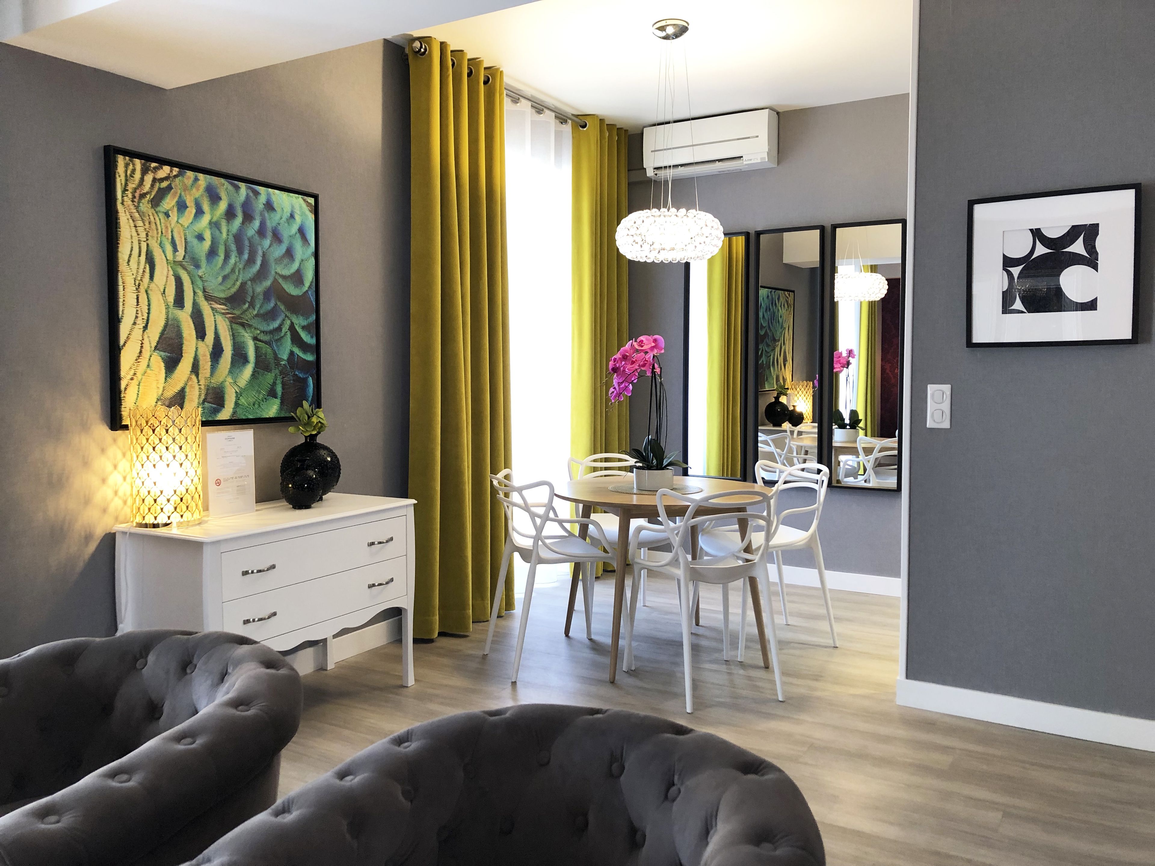 A modern living room with a dining area, featuring a tufted sofa, a dining table with chairs, and a chandelier.
