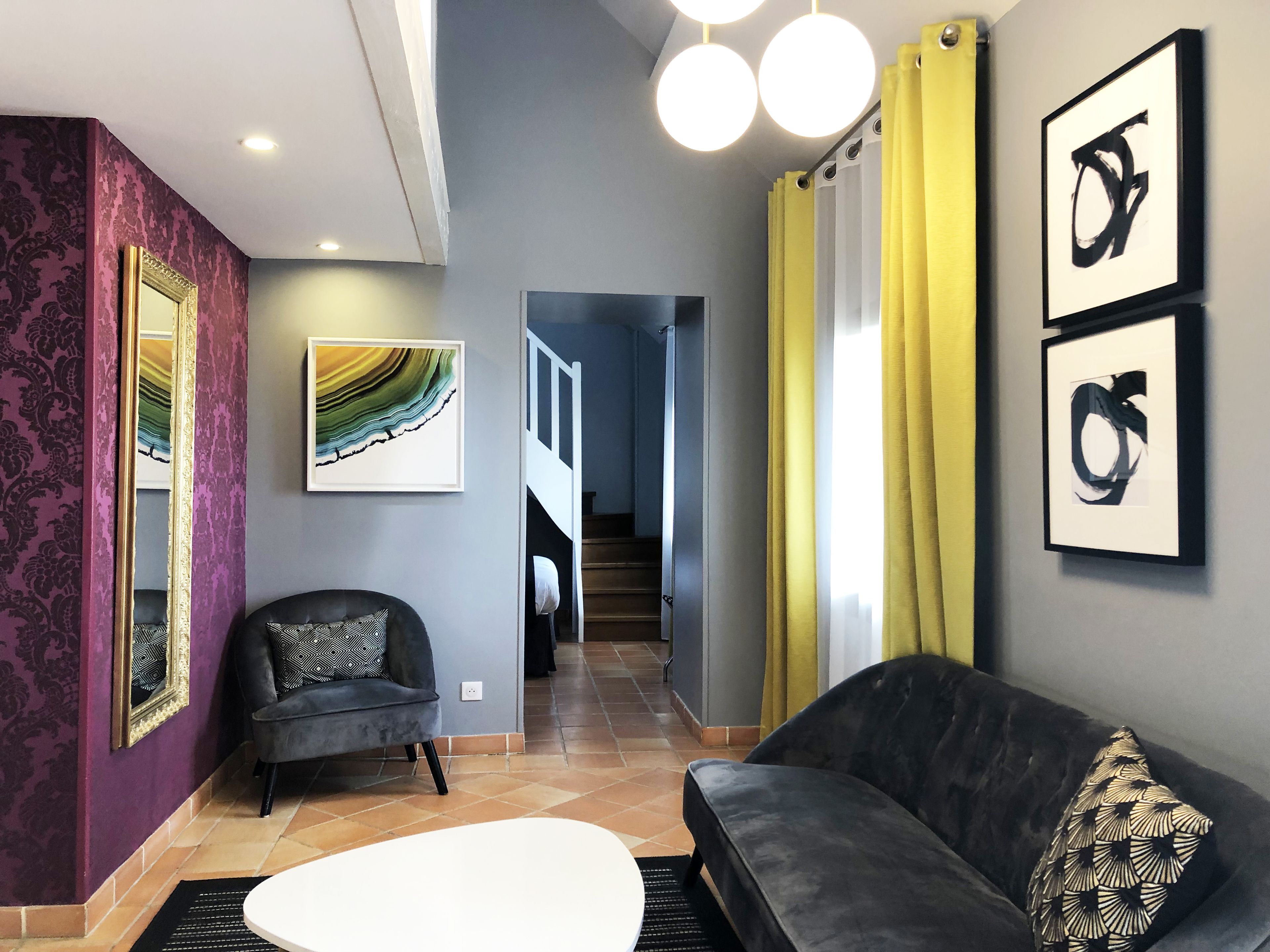A modern living room with a grey sofa, a black armchair, and a white coffee table. There are framed artworks on the walls and a staircase leading to another level.