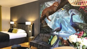 A hotel room with a bed, a sofa, a coffee table, and a large wall mural of a leopard and peacock. - Hotel Les Suites - De Crécy (Crecy-la-Chapelle)