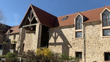 A stone building with a red roof, large windows, and a courtyard with outdoor seating.