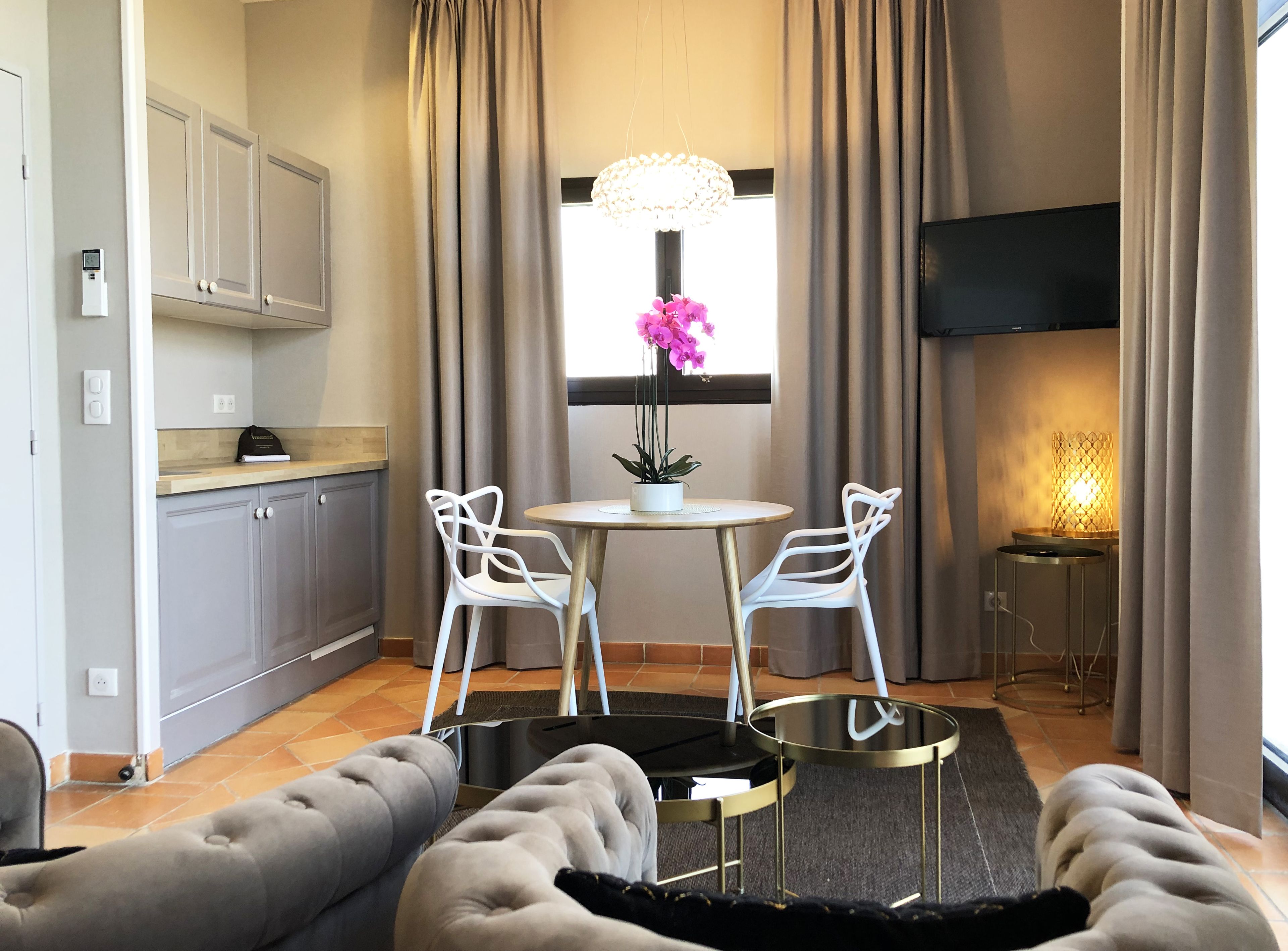 A modern living room with a round table, two white chairs, a sofa, a TV, and a window with curtains.