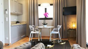 A modern living room with a round table, two white chairs, a sofa, a TV, and a window with curtains.