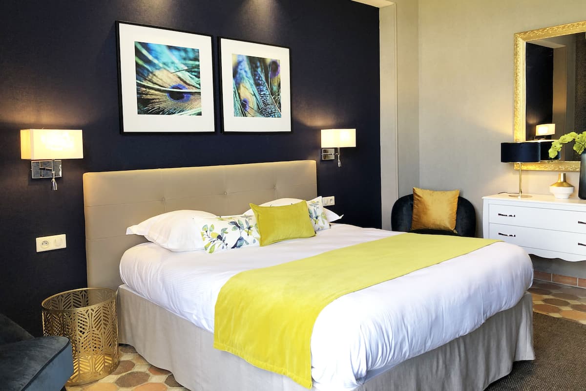 Habitación de hotel con una cama grande, dos lámparas de pared, una mesita de noche con lámpara, un espejo y dos cuadros enmarcados.