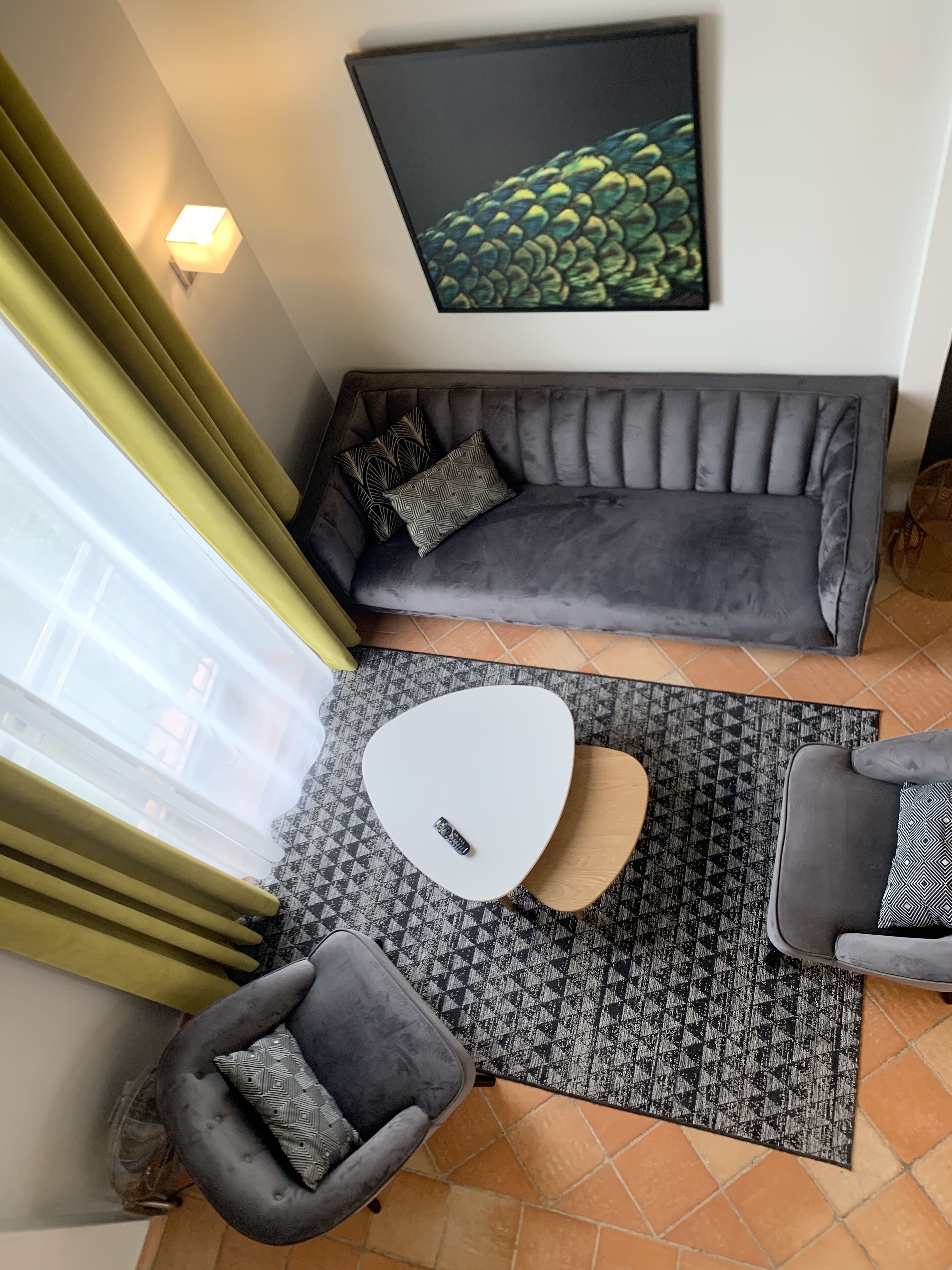 A modern living room with a grey sofa, a white coffee table, and a grey armchair. A patterned rug covers the floor, and a painting is on the wall.