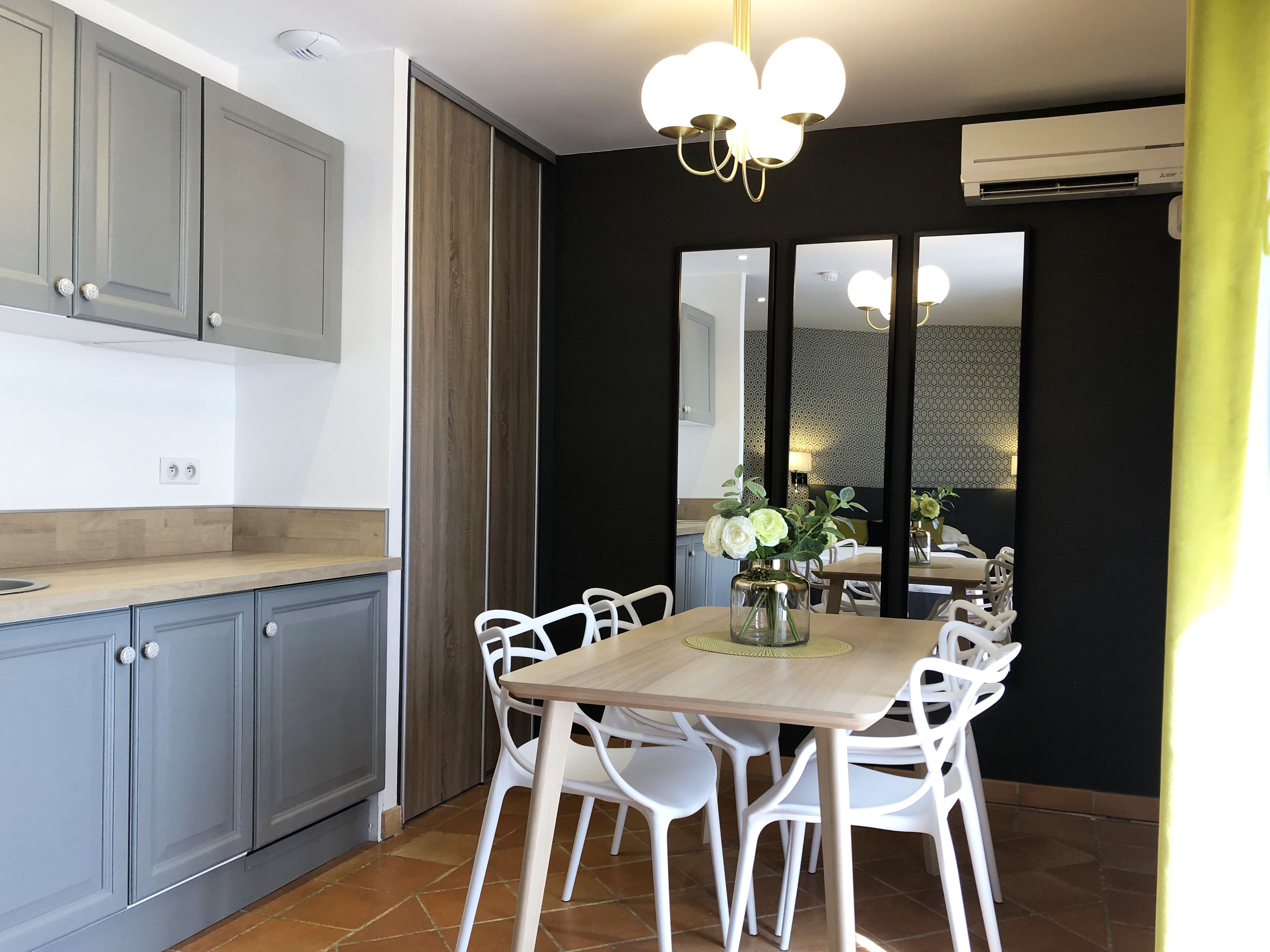 A modern kitchen with grey cabinets, a wooden countertop, and a dining area with a wooden table and white chairs.