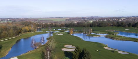 Ein Golfplatz mit mehreren Teichen und Sandbunkern, umgeben von Bäumen und einer in der Ferne liegenden Stadt.