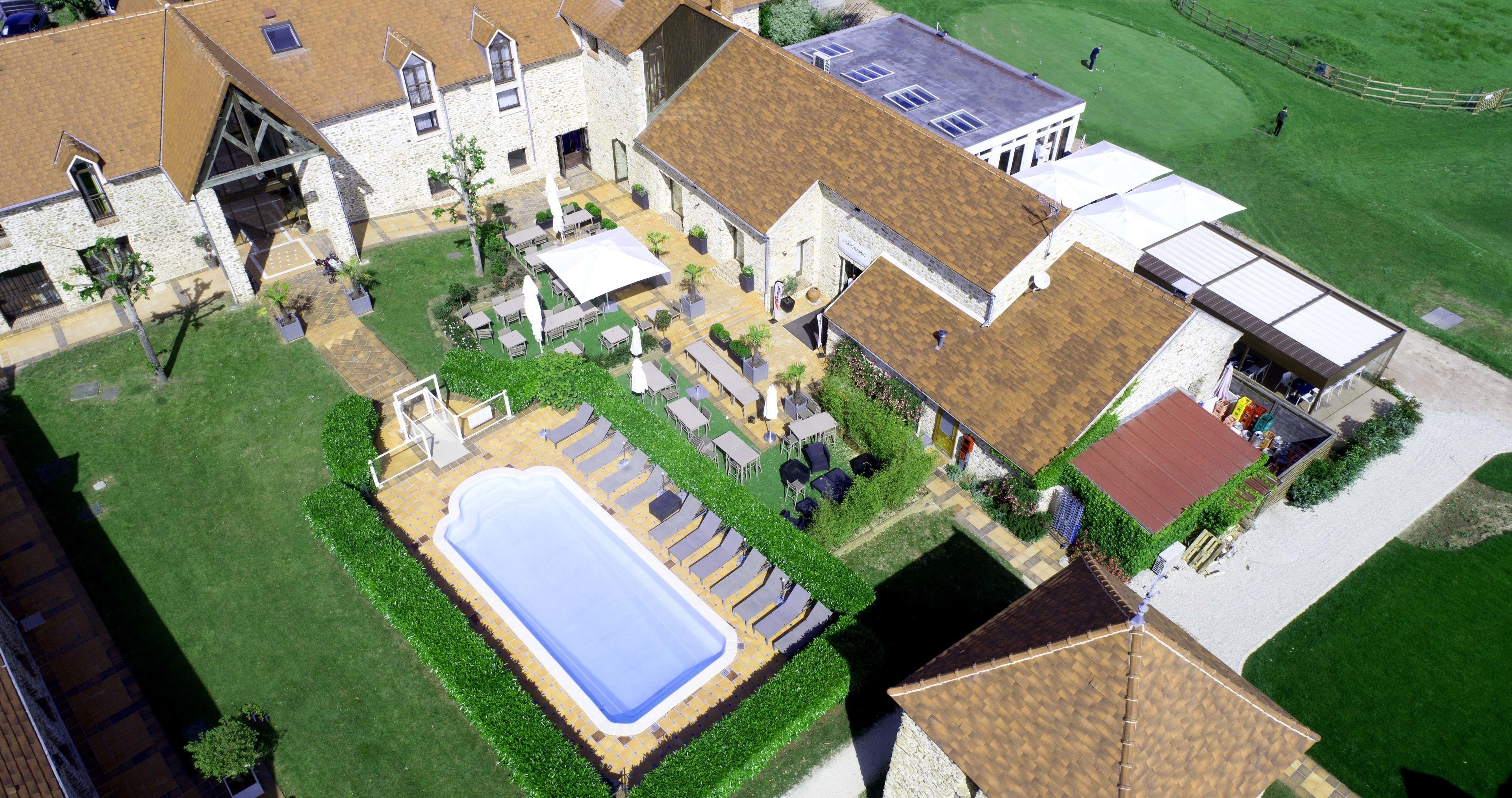 An aerial view of a property with a swimming pool, outdoor seating, and a well-maintained lawn.