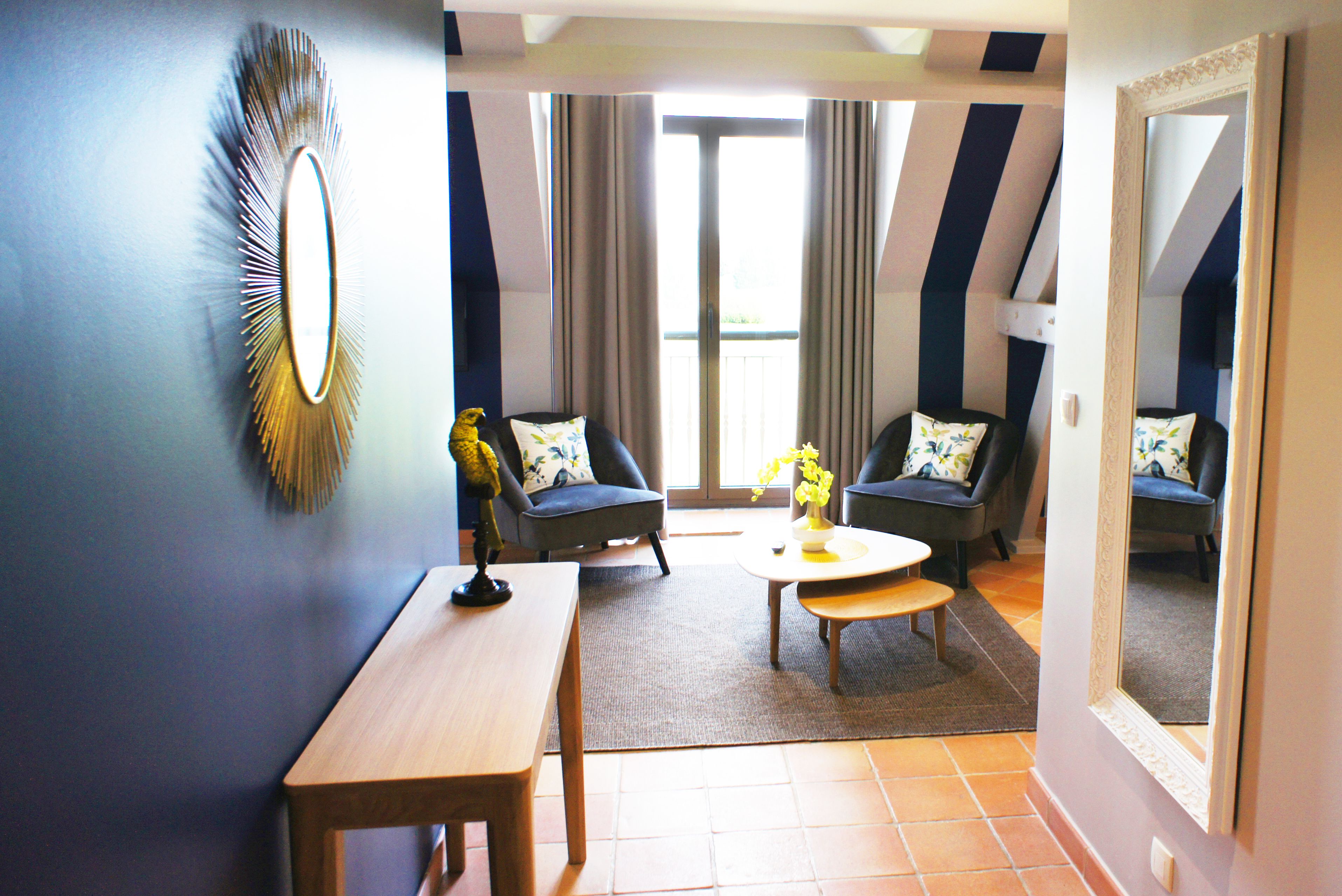 A modern living room with a large mirror, two armchairs, a coffee table, and a wooden bench.