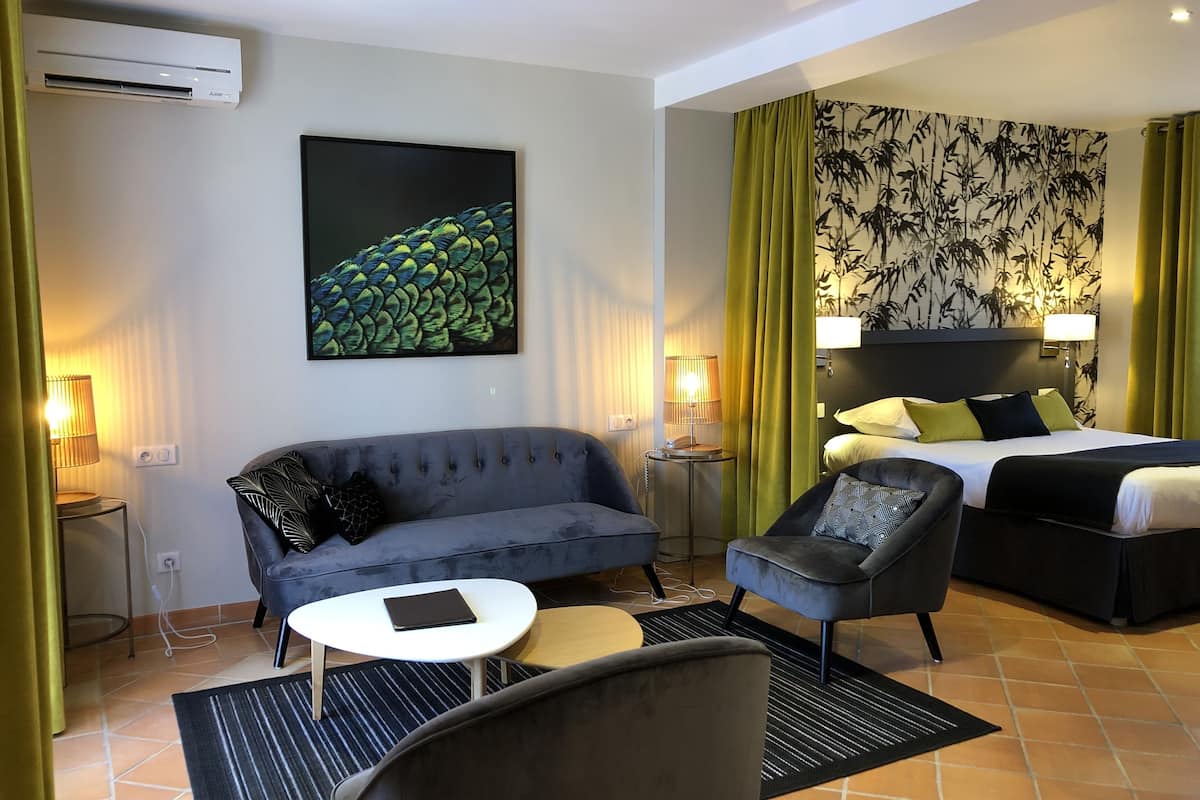 Habitación de hotel con sofá, sillón, mesita redonda y cama con cabecera.