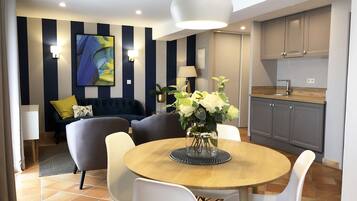 A modern living room with a round wooden table, white chairs, a dark blue sofa, and a large abstract painting on the wall.