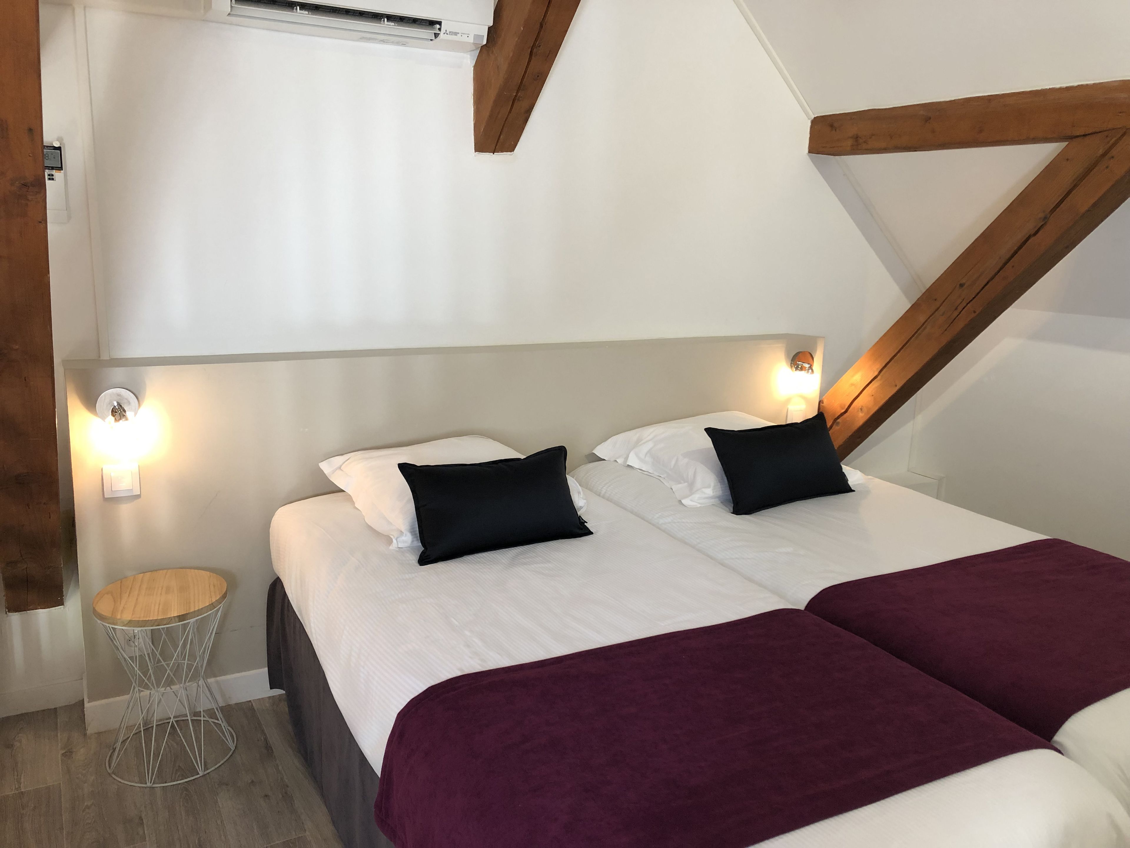 A bedroom with two beds, a round wooden side table, and a wall-mounted air conditioner.