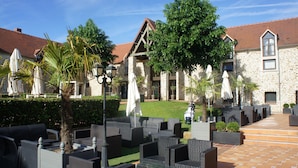 A courtyard with outdoor seating, a stone building, and a well-maintained lawn. - Hotel Les Suites - De Crécy (Crecy-la-Chapelle)