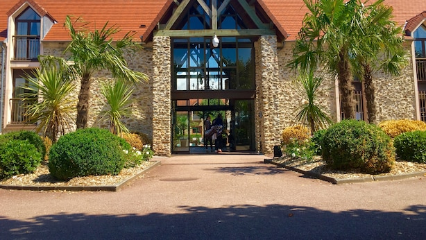 A hotel entrance with a stone facade, a red-tiled roof, and a glass entrance. - Hotel Les Suites - De Crécy (Crecy-la-Chapelle)