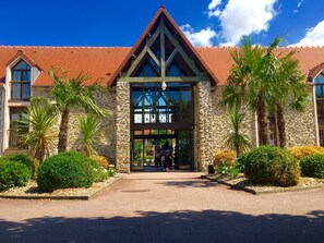 Fachada de hotel de piedra, tejado de tejas rojas y entrada de cristal.