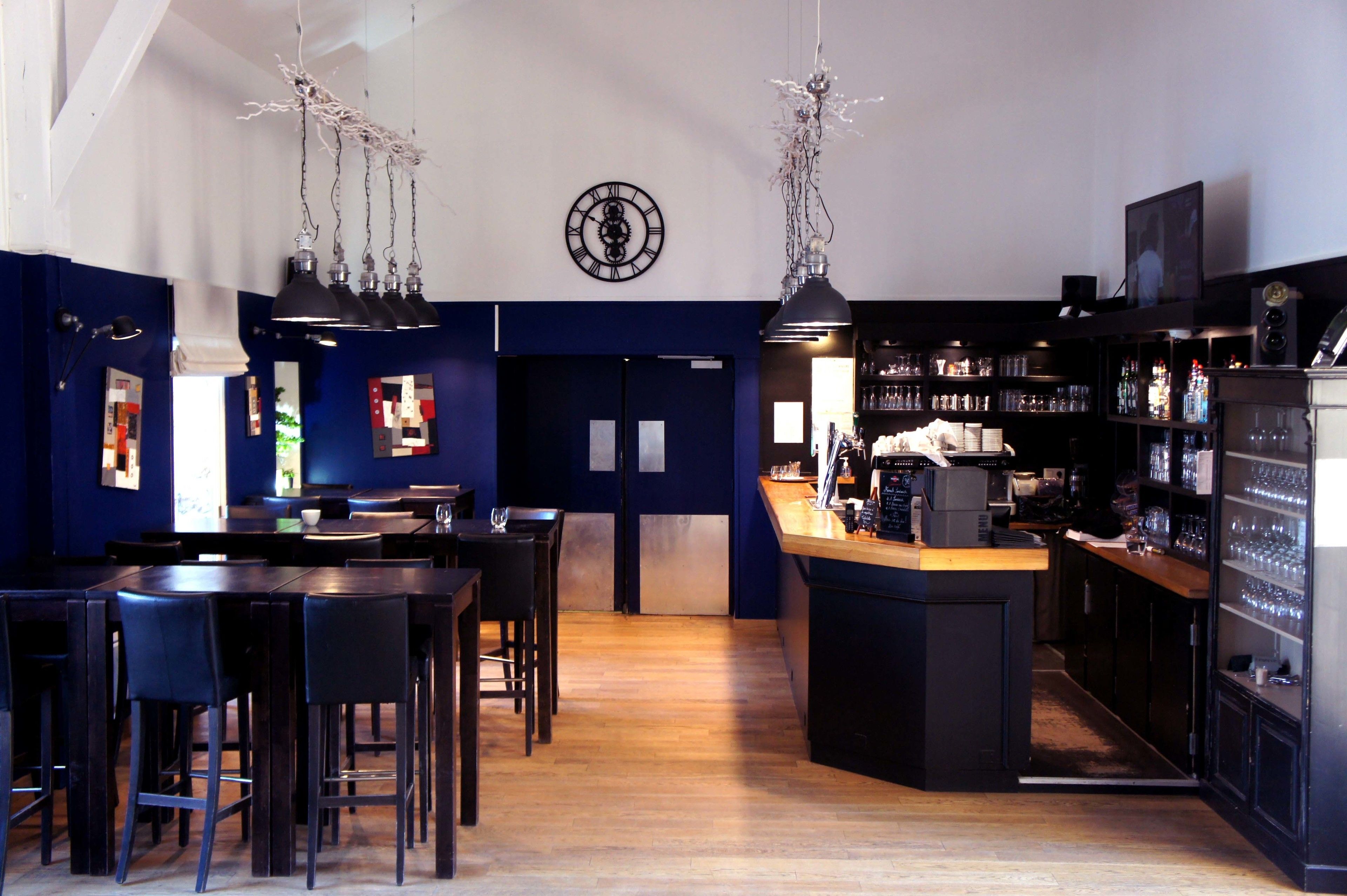 Un espace bar avec des tables et des chaises en bois, un comptoir et des étagères remplies de bouteilles et de verres.