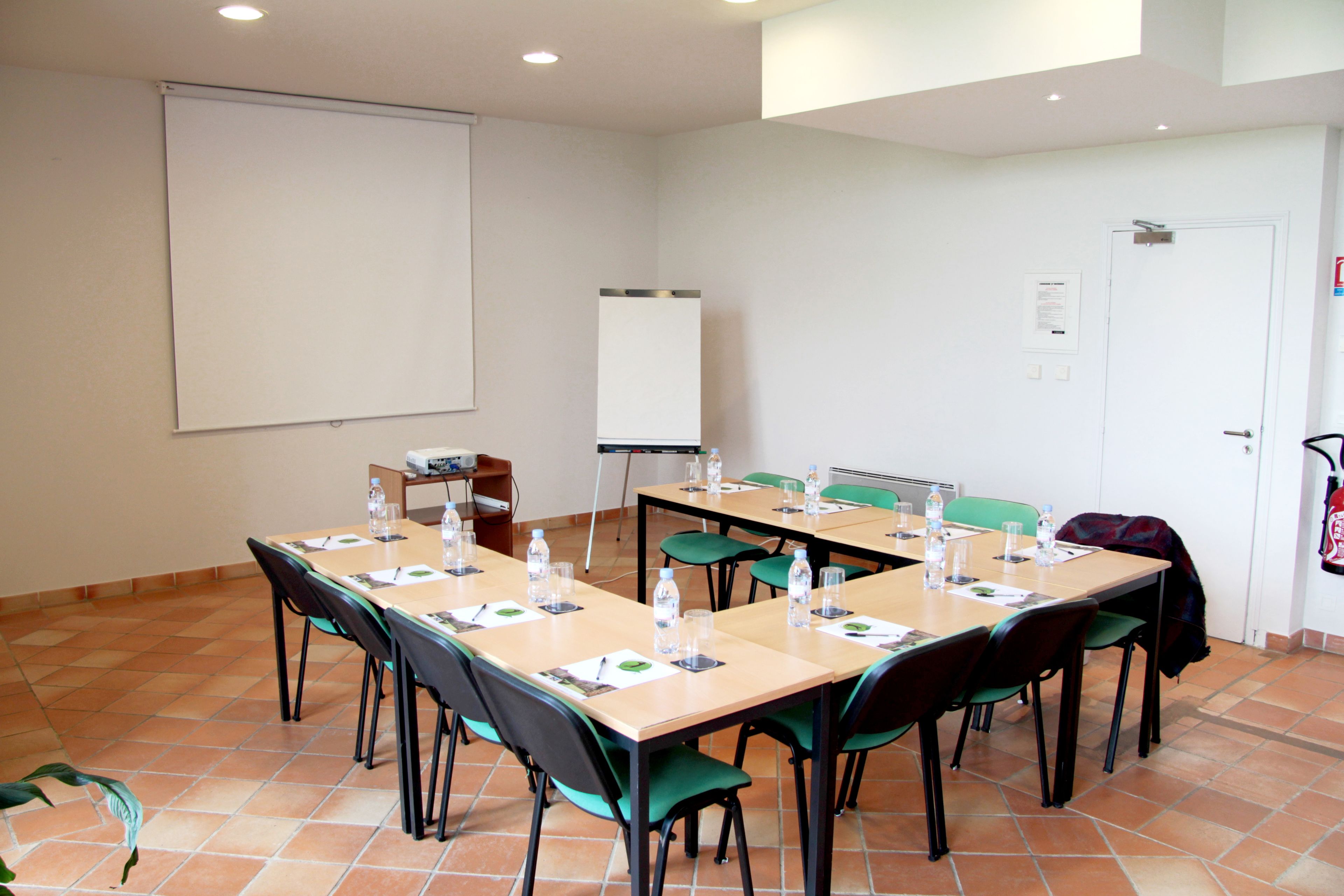 Un salón de conferencias con una gran mesa, sillas, una pantalla de proyector y una pizarra.