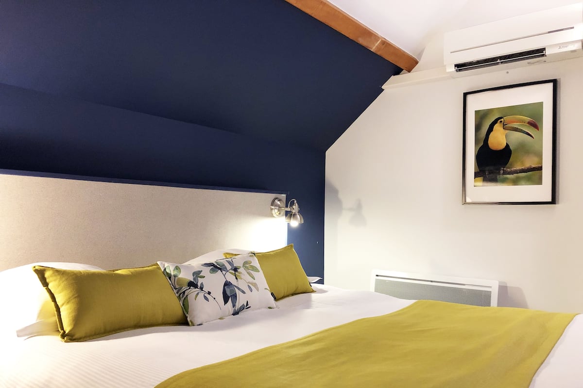 Un dormitorio con cama, almohadas, una lámpara de pared y un cuadro enmarcado.