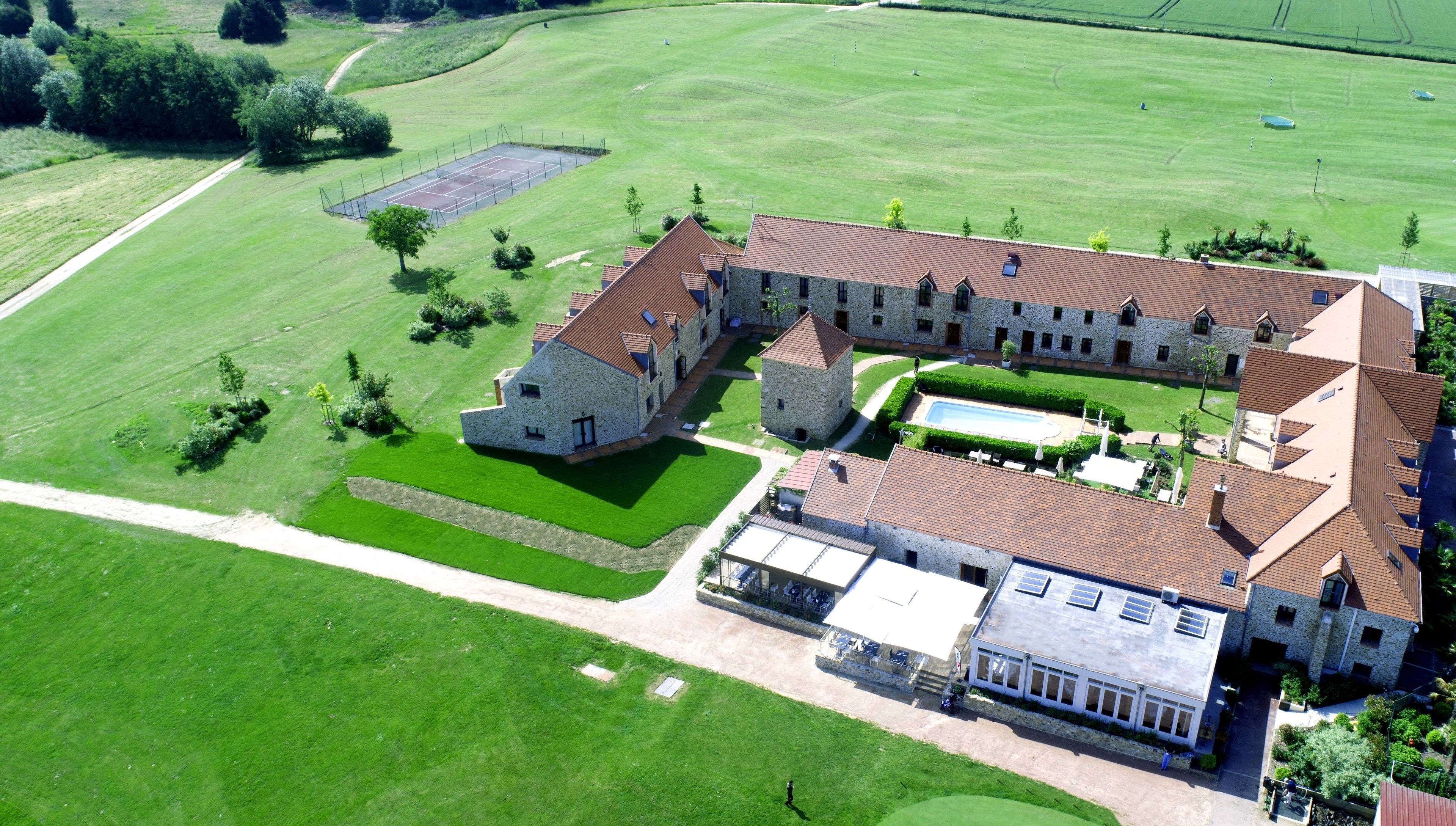 Vista aérea de una extensa propiedad con varias edificaciones, incluyendo una casa principal con fachada de piedra, una piscina y céspedes bien cuidados.