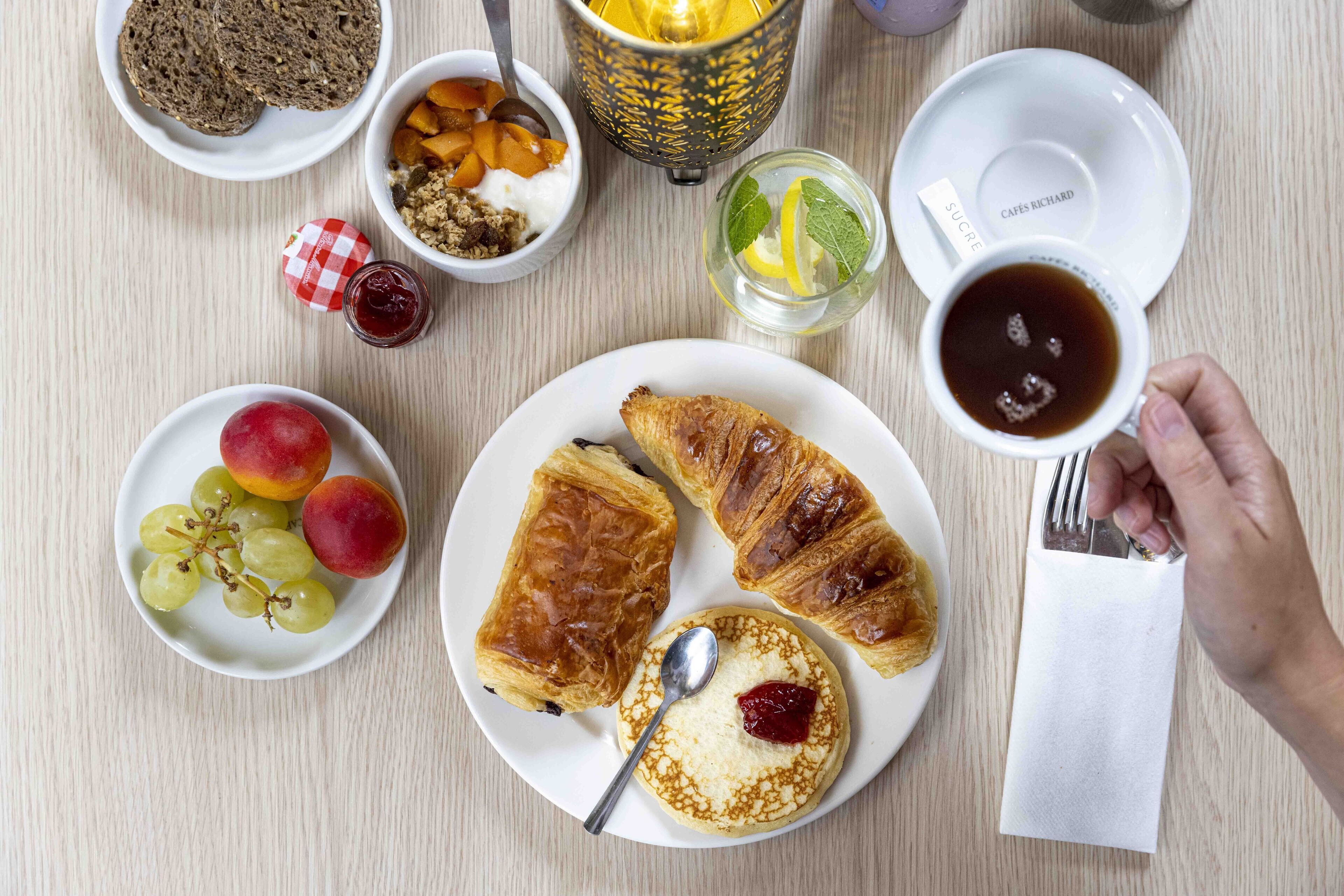 A breakfast setting with croissants, fruit, yogurt, and coffee on a wooden table.