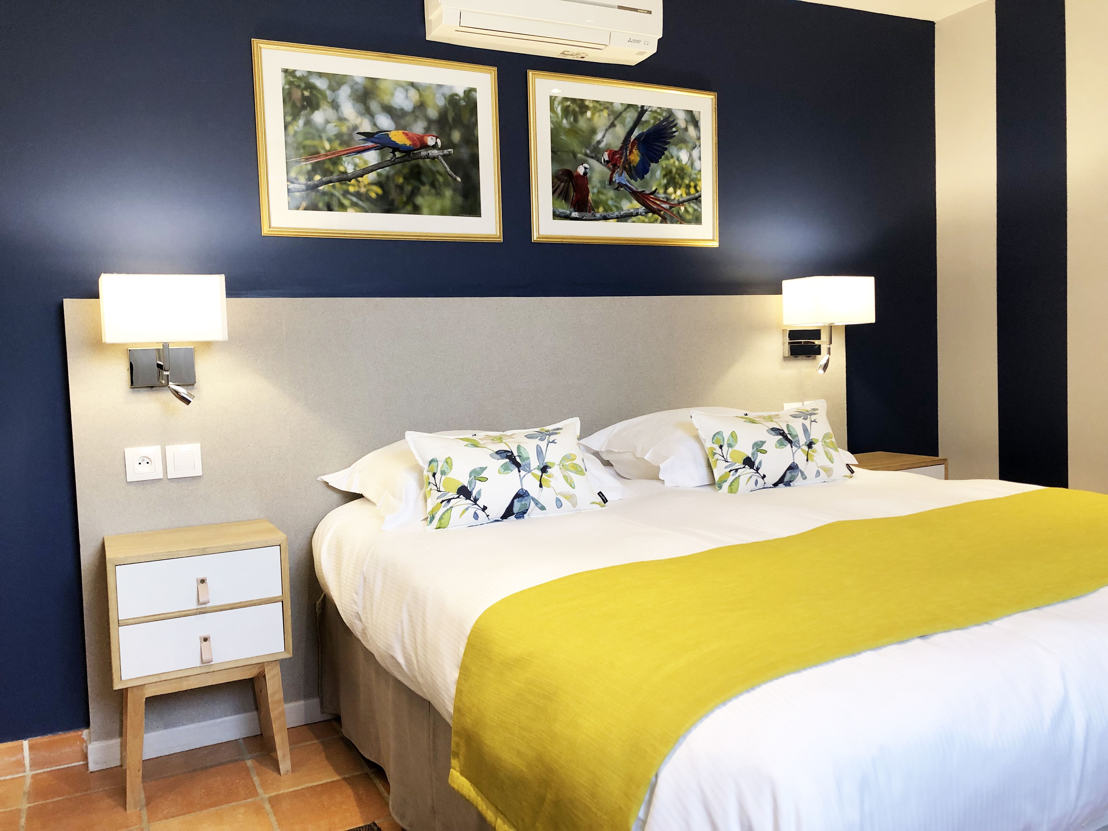 Een hotelkamer met een bed, twee nachtkastjes, een bedtafel, een lamp en twee ingelijste foto's aan de muur.