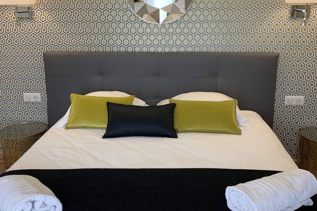 Una cama bien hecha con una pared de estampado geométrico y un espejo grande y circular encima.