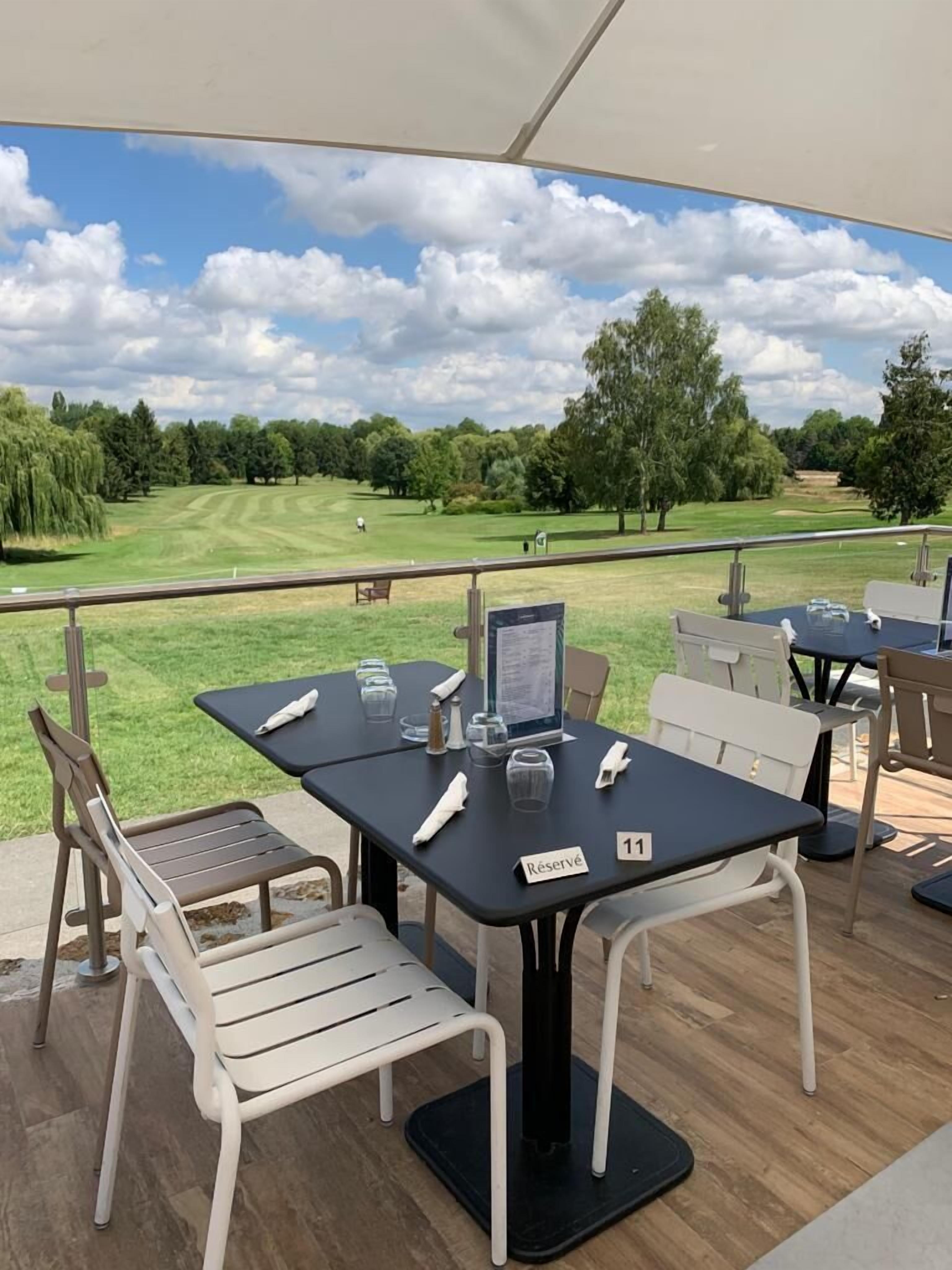 Un espace extérieur aménagé avec des tables et des chaises, une vue sur un terrain de golf et un panneau indiquant qu’une table est réservée.