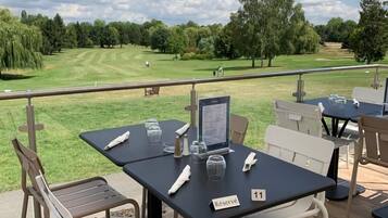 Un espace extérieur aménagé avec des tables et des chaises, une vue sur un terrain de golf et un panneau indiquant qu’une table est réservée.