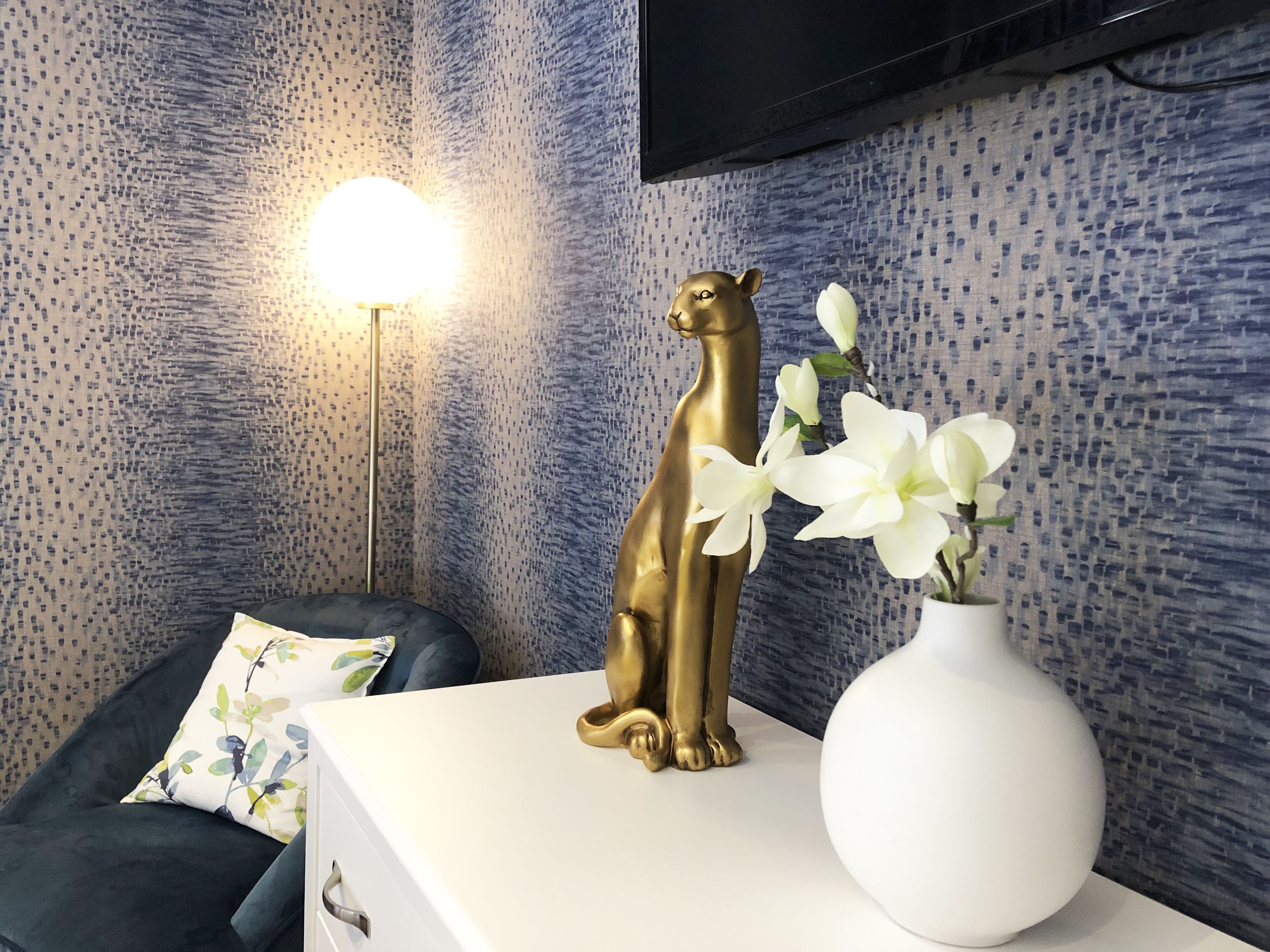 A room with a white dresser, a gold animal figurine, and a white vase with flowers.