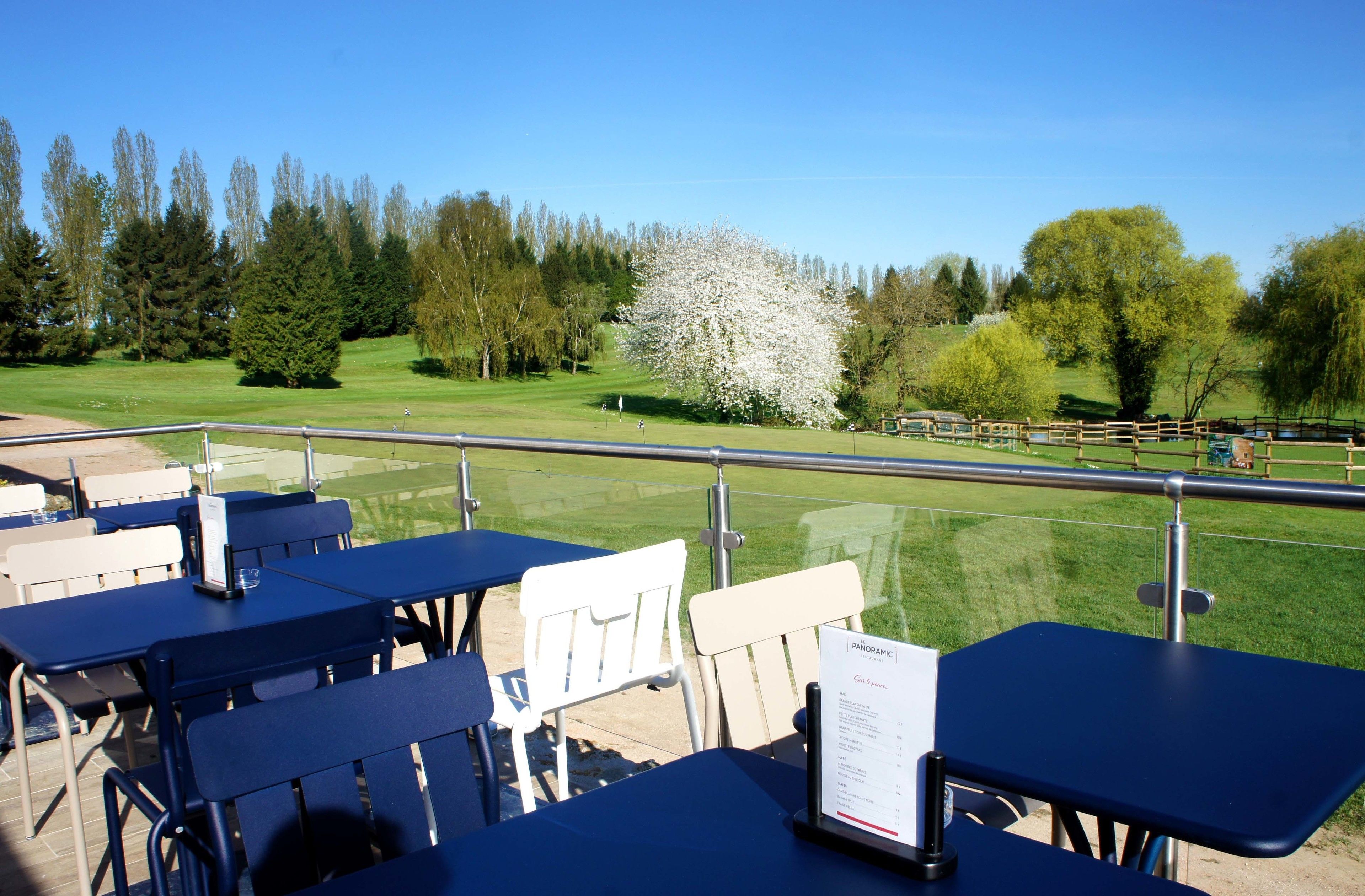 A terrace with tables and chairs overlooking a golf course.