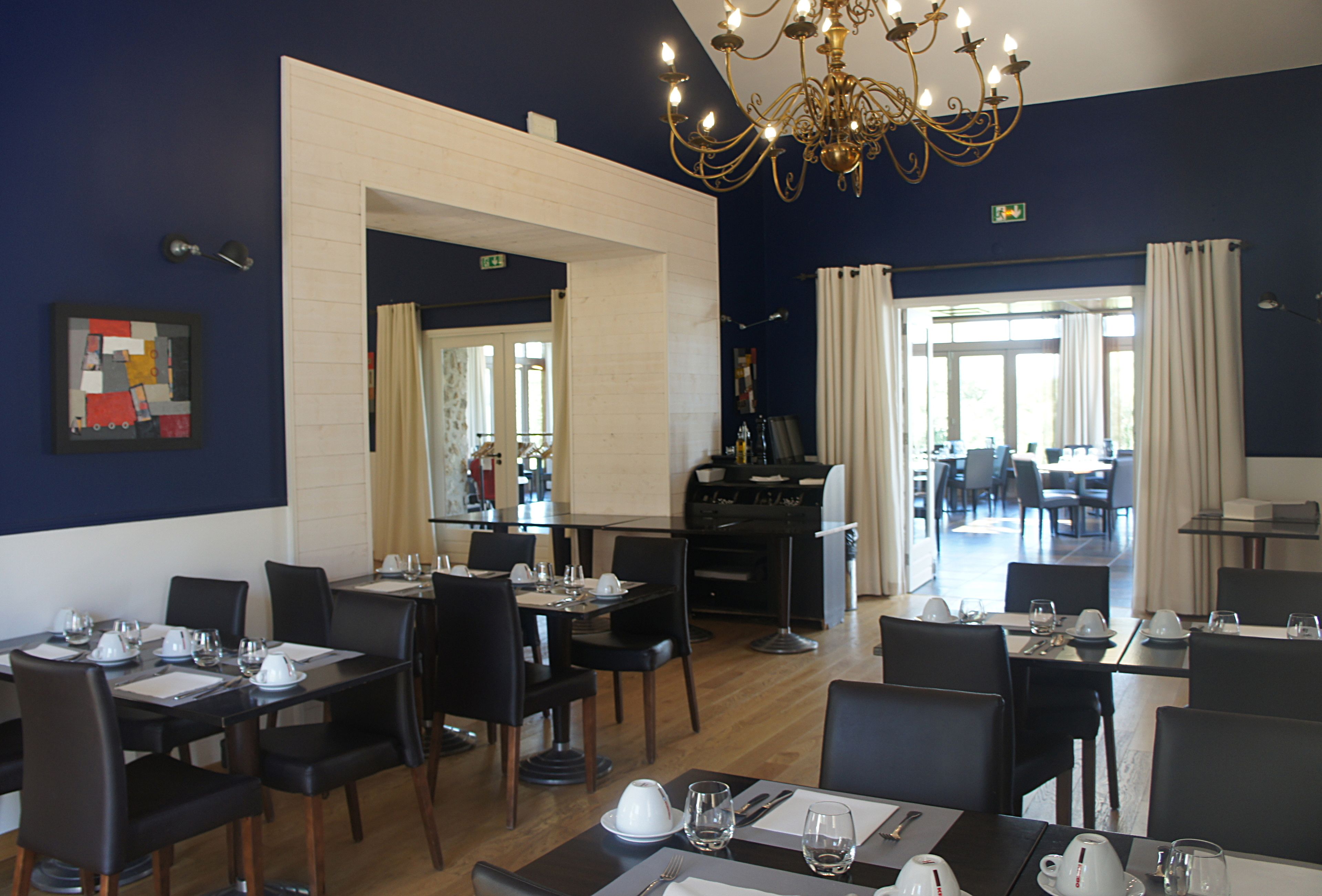 A hotel dining area with tables set for service, a chandelier, and a view into the dining room.