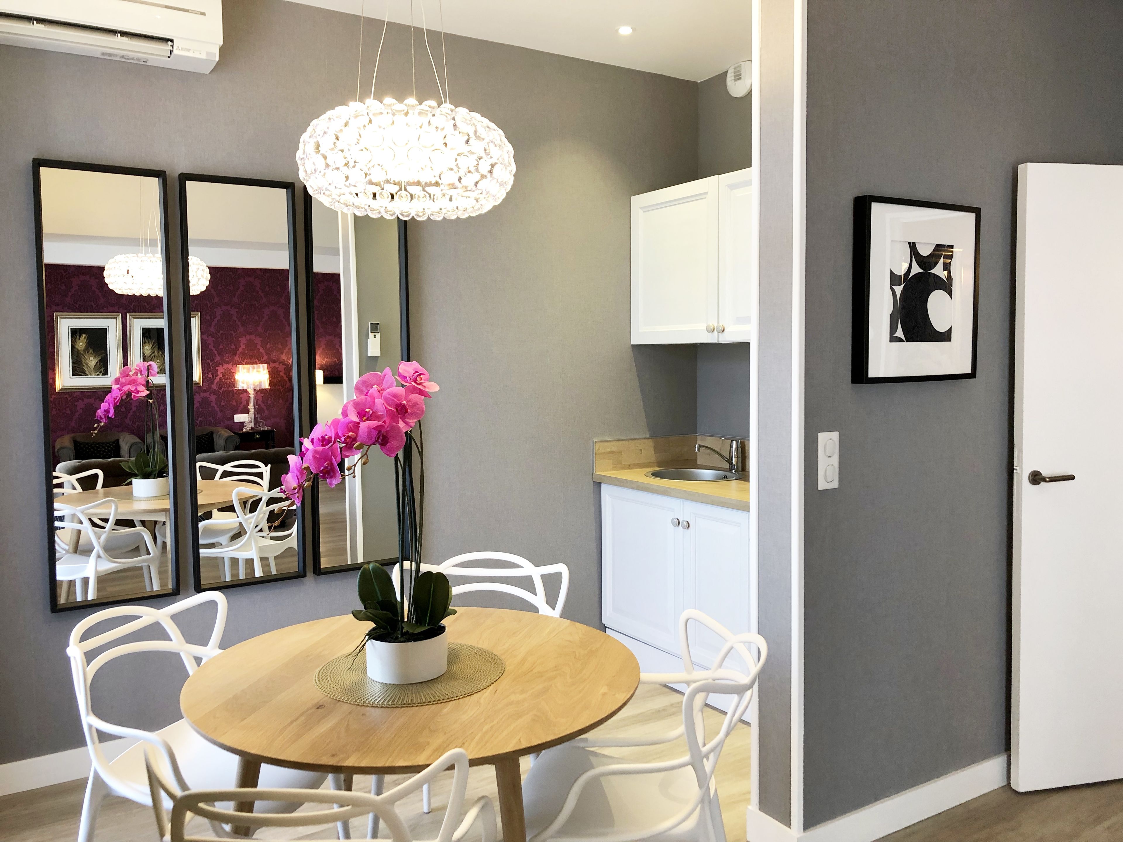 A modern dining area with a round wooden table, white chairs, and a central orchid plant.