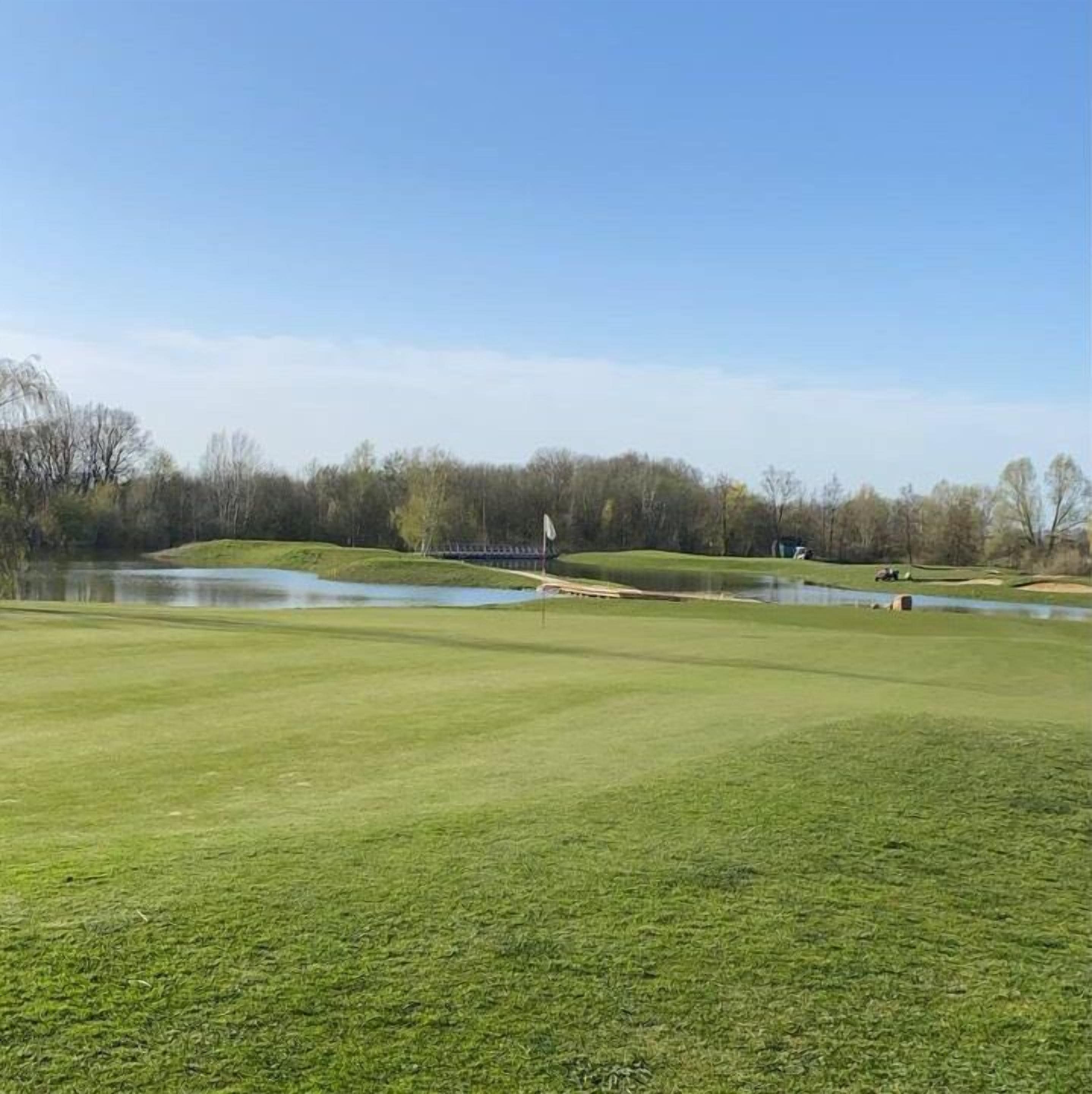 Een golfbaan met een vijver, bomen en een heldere lucht.