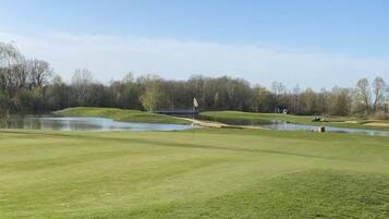Een golfbaan met een vijver, bomen en een heldere lucht.