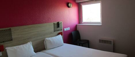 A hotel room with two beds, a red wall, a window, and a chair.