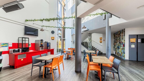 A modern indoor space with a red counter, multiple tables and chairs, a staircase, and a wall decorated with pictures.