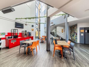 A modern indoor space with a red counter, multiple tables and chairs, a staircase, and a wall decorated with pictures. - hotelF1 Strasbourg La Vigie (Ostwald)
