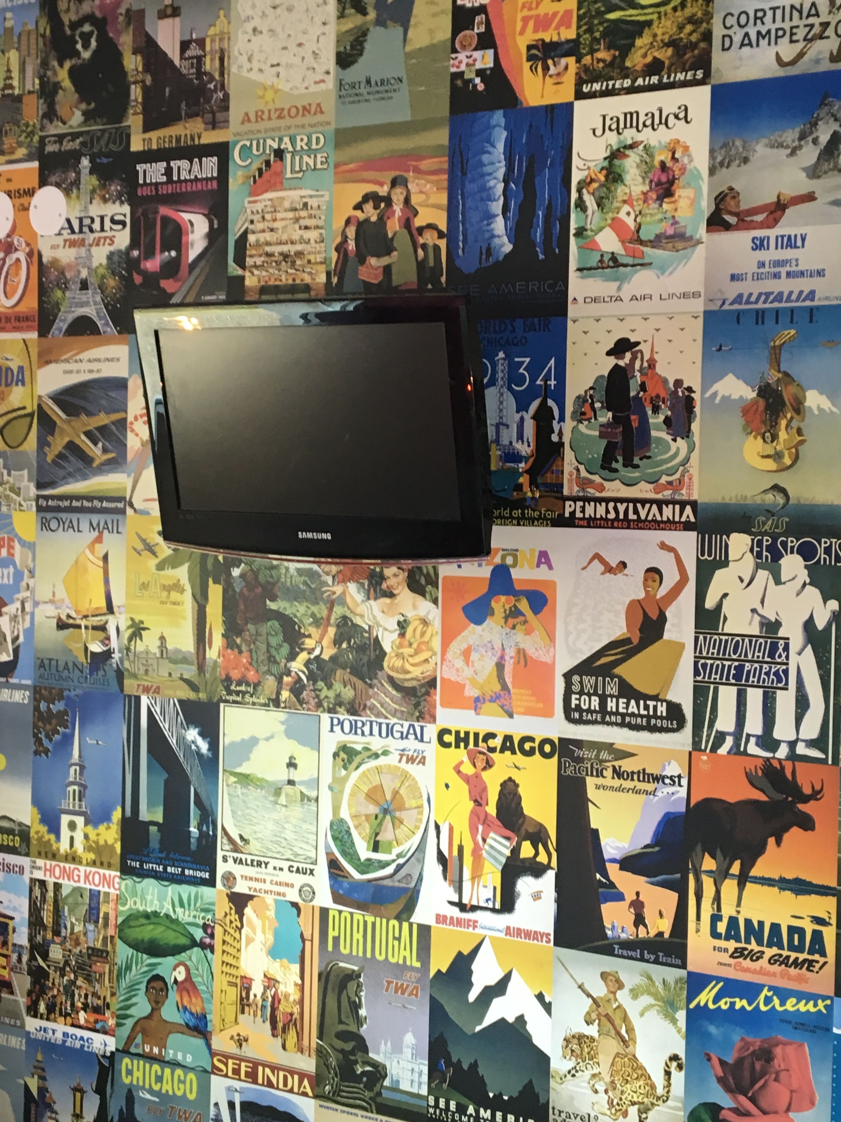 A wall covered with various travel posters and a Samsung TV mounted on it.