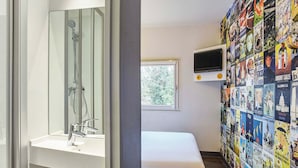 A bathroom with a shower, sink, and bench. There is a window and a wall with travel posters.