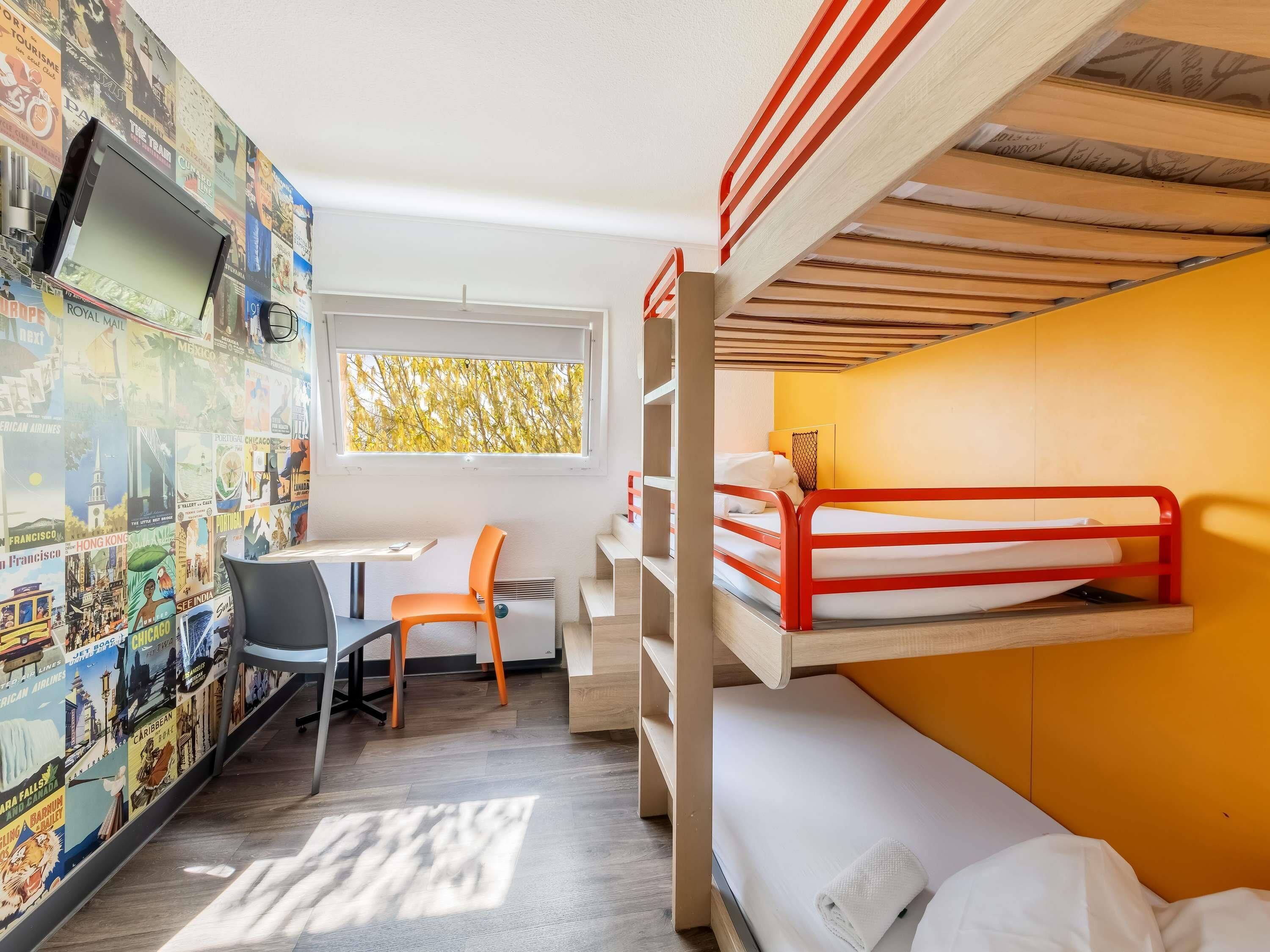 Ein Zimmer mit Etagenbett, Schreibtisch, Stuhl und einer Wand mit Reiseplakaten.