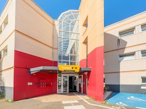 A hotel entrance with a glass facade, a red and beige exterior, and a wheelchair-accessible parking area. - hotelF1 Strasbourg La Vigie (Ostwald)