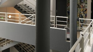A multi-level interior with a staircase, columns, and a wall decorated with posters.