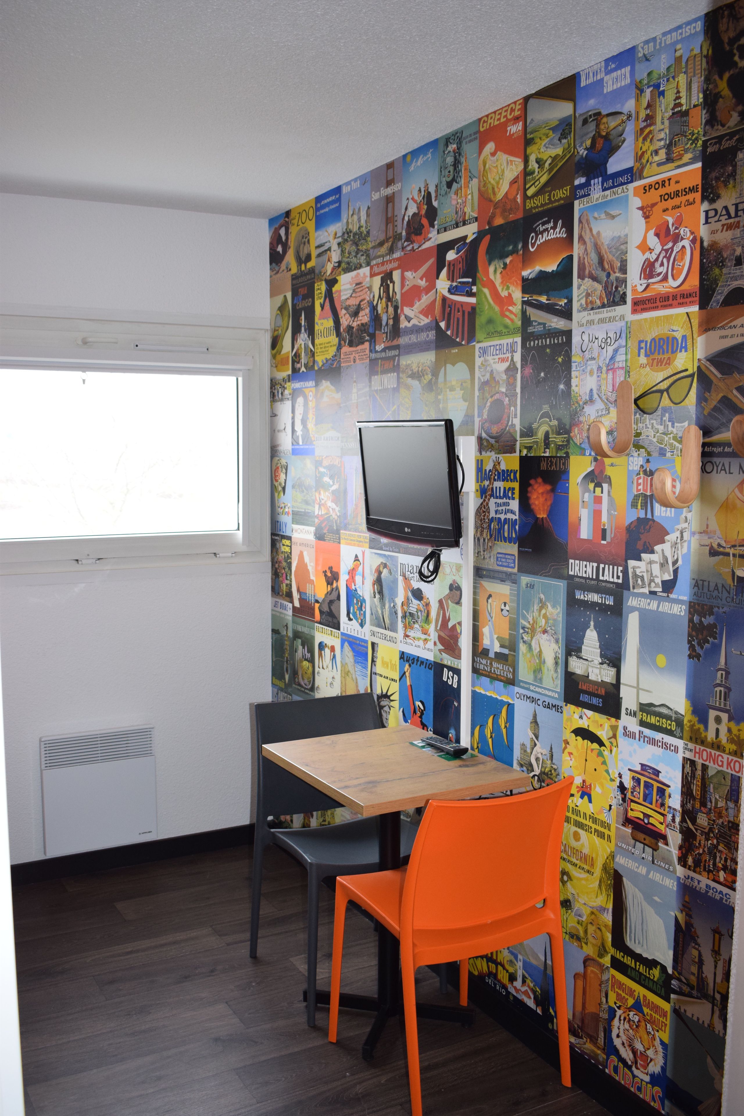 A room with a desk, two chairs, a television, and a wall covered with travel posters.