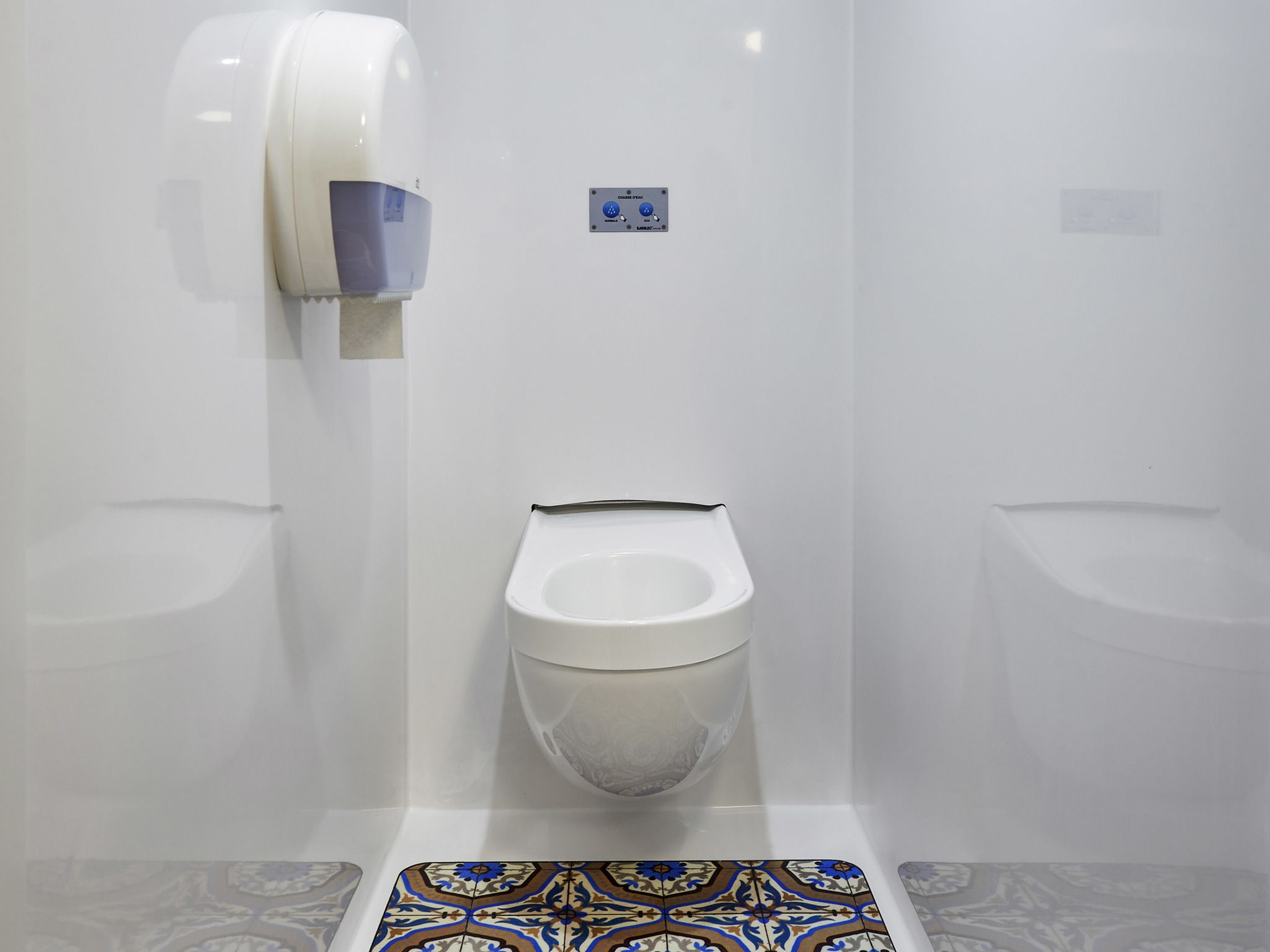 Un baño moderno con orinal, secamanos y suelo de baldosas.