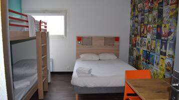 Habitación tipo dormitorio con literas, una cama individual, una mesa de madera y un muro decorado con carteles de colores.