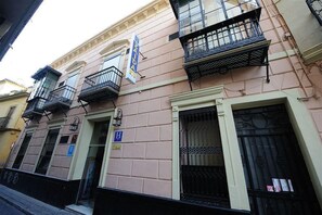 A building with multiple balconies, a blue sign indicating a hotel, and a visible entrance door. - Zaida (Seville)