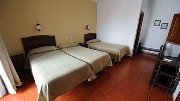Habitación de hotel con dos camas individuales, una mesita de noche de madera con lámpara, una pequeña mesa con una silla y un armario.