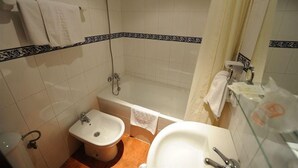 A bathroom with a bathtub, a sink, and a bidet. There are towels hanging on the wall and a shower curtain. - Zaida (Seville)