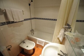 A bathroom with a bathtub, a sink, and a bidet. There are towels hanging on the wall and a shower curtain. - Zaida (Seville)