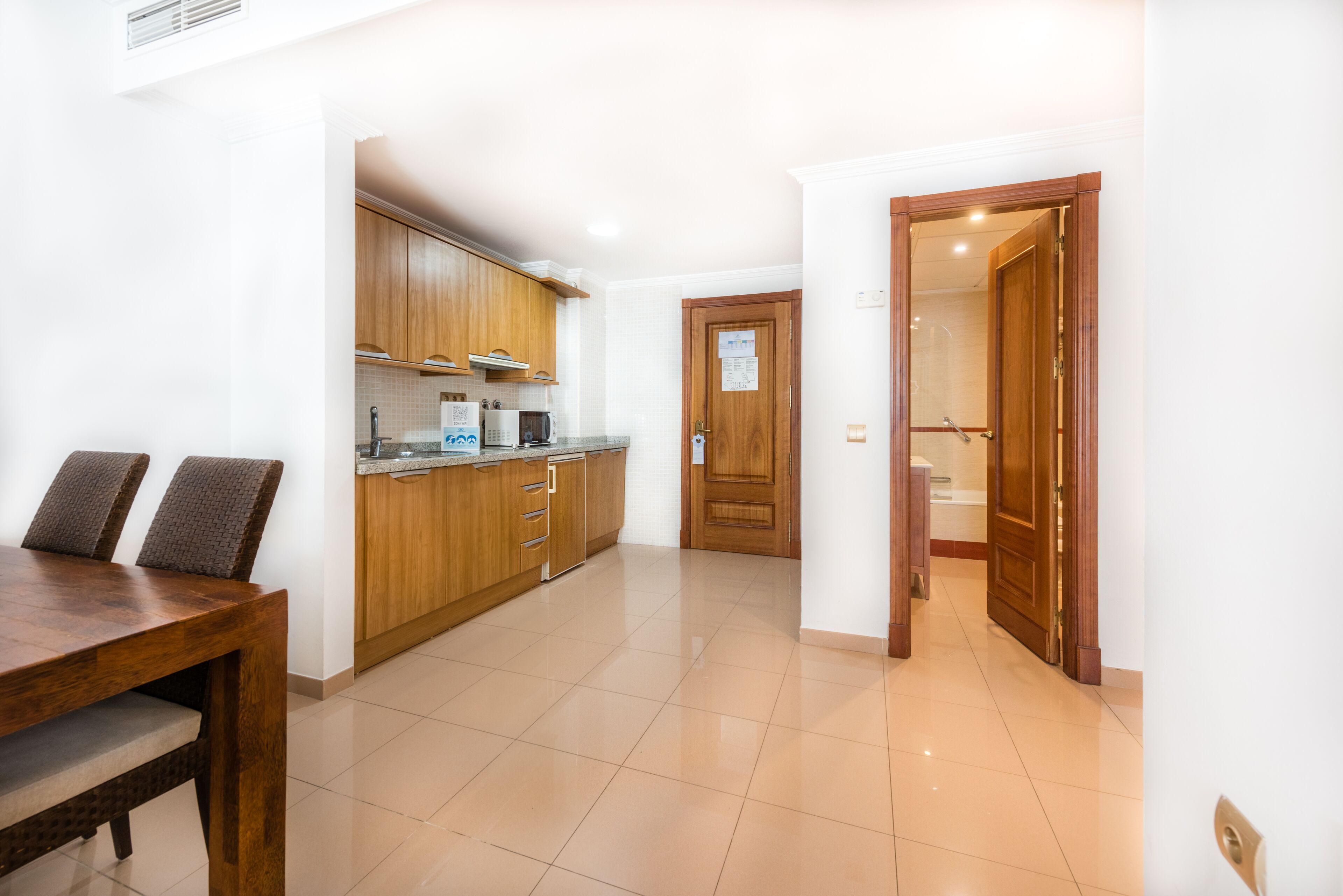 A modern kitchen with wooden cabinets, a dining table with chairs, and a tiled floor.
